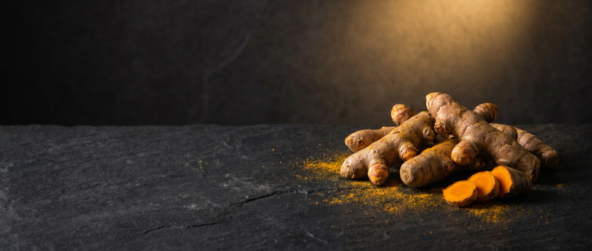Whole turmeric root on a dark stone surface.